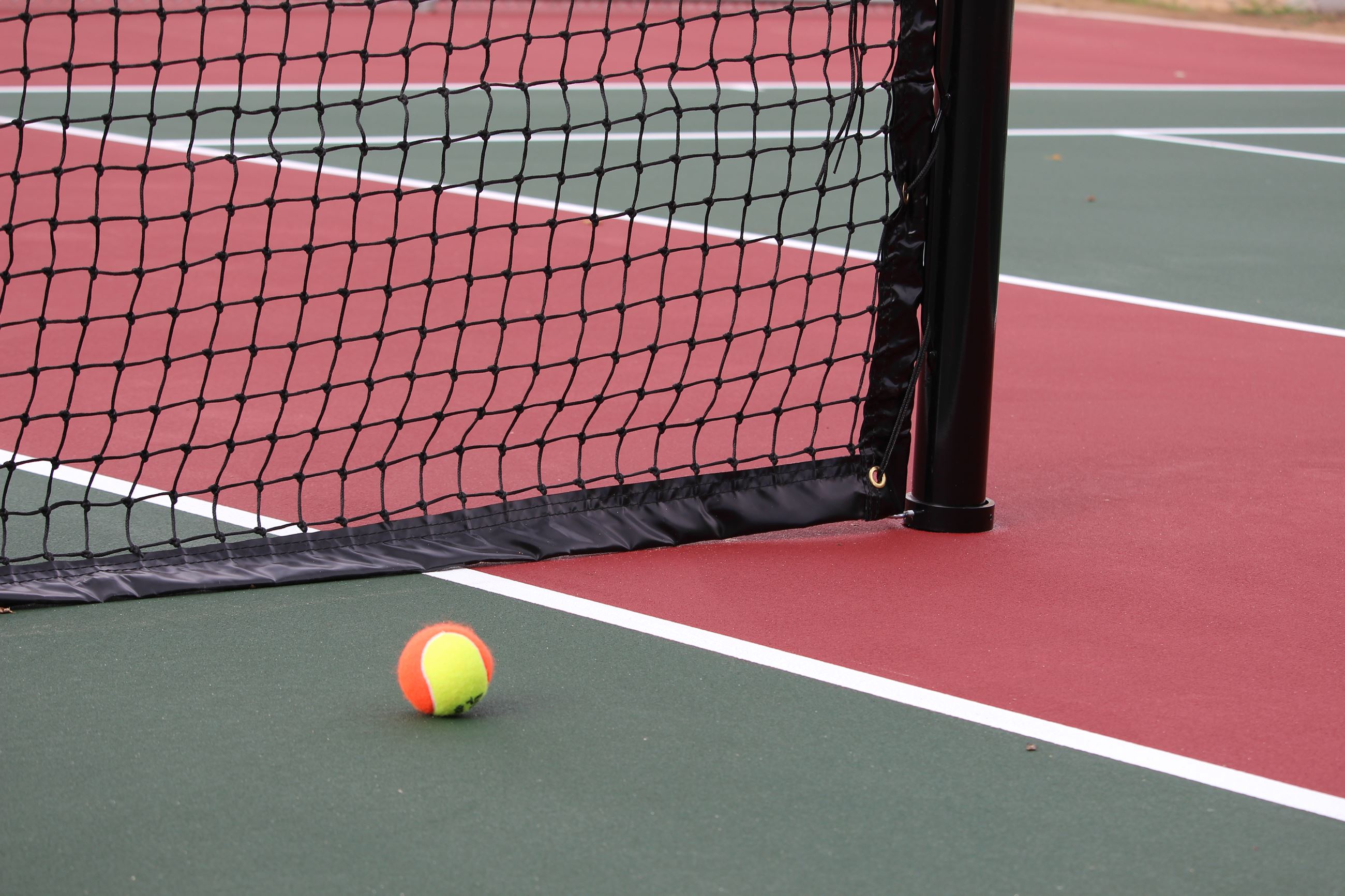 A tennis ball sitting on the court next to the net